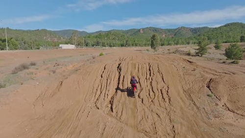 Motocross rider speeds through a dusty, rugged off-road track with mountains