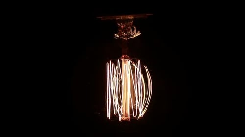 Illuminated Vintage Lightbulb Filament Against Black Background