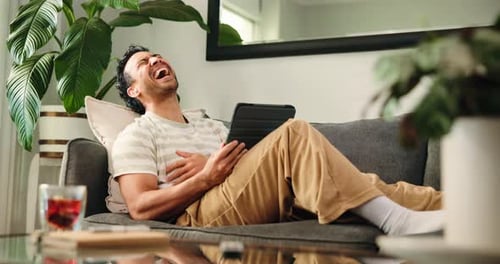 Man Laughing While Looking at Tablet on Couch