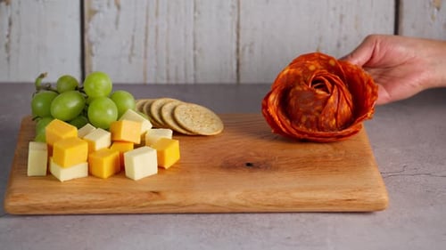 Planche à charcuterie, préparant un plateau de fromages, une main place une rose au pepperoni sur un plateau de fromages