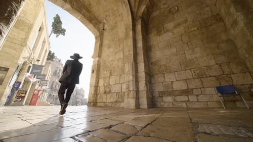 Man in Black Suit Walks Through Stone Archway