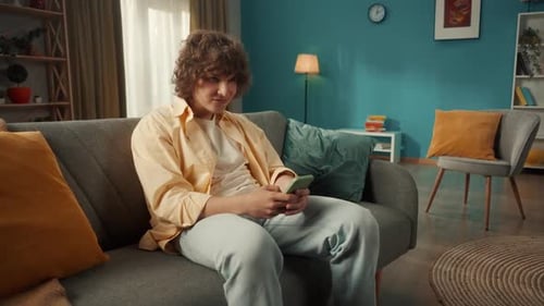 Curly-Haired Young Adult Using Smartphone on Couch