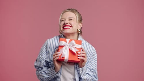 Excited woman holding a wrapped gift against pink backdrop