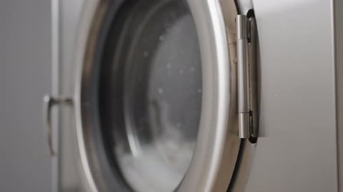 Close Up Washing Machine Door with Soap Water and Clothes Tumbling