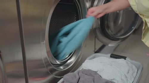 Arbeiter ziehen in einem modernen Waschsalon mit der Hand das Tuch aus dem Trockner in den Korb