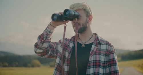 Blonder Mann schaut durch das Fernglas gegen den Himmel