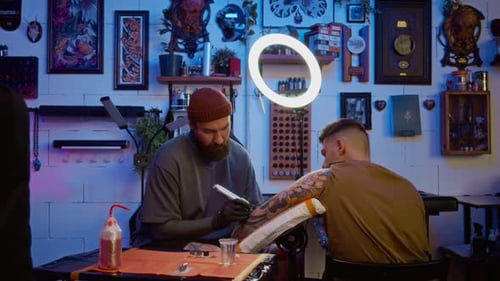 Stylish Male Tattoo Specialist Creating Body Art on Clients Arm in Modern Studio