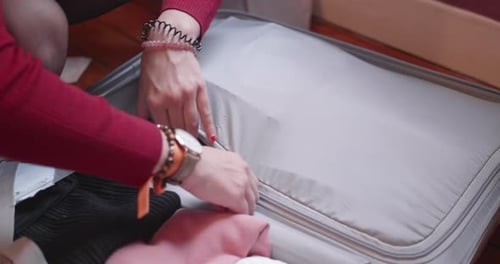 Close up of hands packing a suitcase then trying to close the zipper, with difficulty. Professional