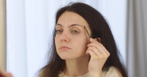 Woman Applying Eyebrow Makeup in Mirror