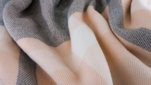 Top view of the soft folds of wool fabric in pastel gray-pink colors rotated on the display case.