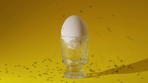 Osterei auf dem Eierständer, das mit glänzendem Glitzer auf gelbem Hintergrund übergossen wird