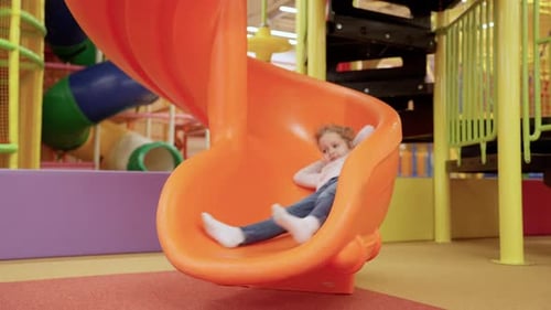 Girl Slides Down Bright Orange Indoor Playground Slide
