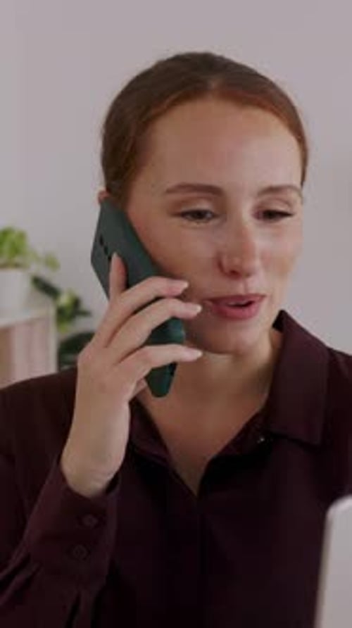 Young Businesswoman Talking on Phone While Working on Laptop at Modern Office