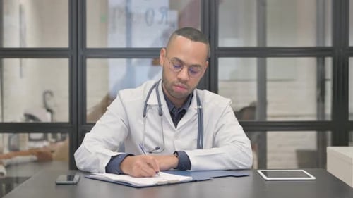 Male Doctor Writing on Clipboard in Office