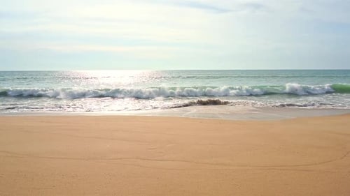 Waves crashing on beach and sunlight reflections on sea surface. Slow-motion