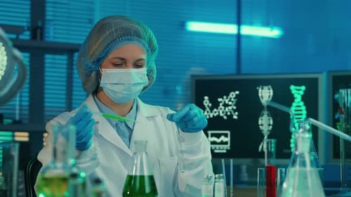 A Female Scientist Pipettes a Green Liquid Into a Glass Test Tube and Examines the Sample