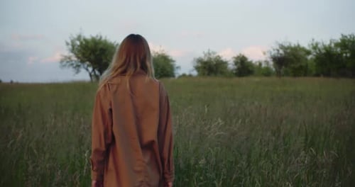 Pretty romantic woman acting on camera walks through a field of tall grass