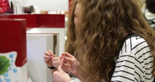 Two Teen Girl Siblings Stand at Makeup Showcase Counter and Hold Lip Gloss