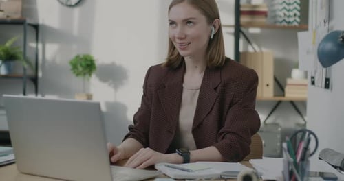 Young Businesswoman Making Online Video Call Using Laptop and Earphones in Office