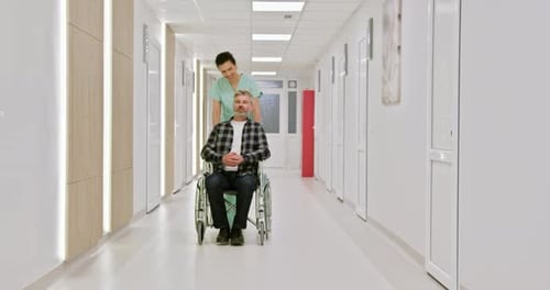 Nurse Assisting Man in Wheelchair in Hospital Corridor
