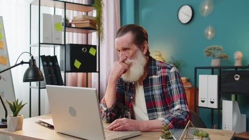 Senior Man Thinking at Laptop in Home Office