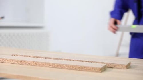 Worker measuring wooden plank with building level at table indoors