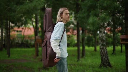 Striding with Purpose Through Botanical City Space As Chords Play Focused Performer Carrying