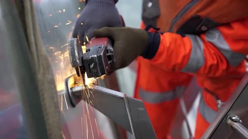 Nahaufnahme eines Arbeiters in orangefarbener Uniform, Hände in Schutzhandschuhen, der mit einem