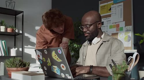 Curly-Haired Guy Asking Male Colleague who Working on Laptop about Project