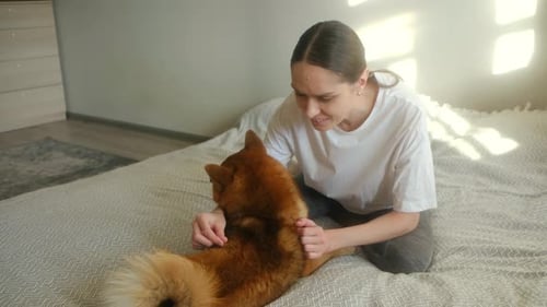 Woman Cuddling Ginger Dog on Bed in Sunny Room