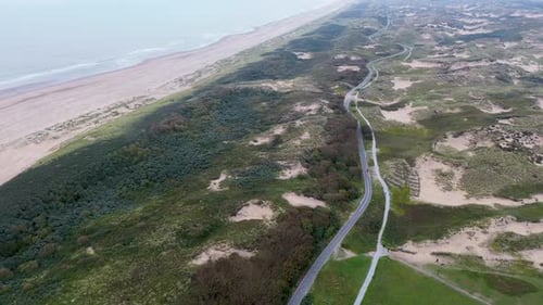 Aerial view of a coastal landscape with lush greenery, sandy dunes, and a winding road running