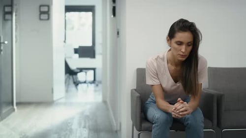 Wide shot of stressed caucasian woman sitting in clinic waiting room and squeezing a stress ball. Sh