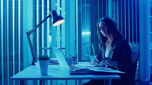 Businesswoman in Stylish Suit Working on Laptop in GlassWalled Office at Night