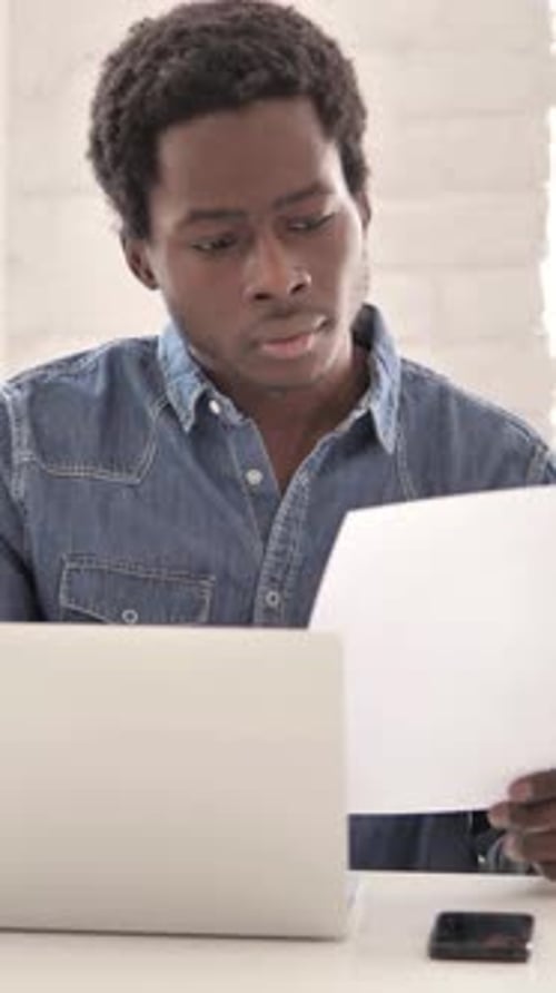 Man Reviews Document at Laptop Inside Home