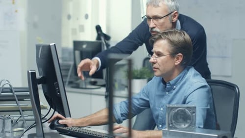 In Busy Engineering Bureau Two Senior Engineers Discussing Technical Issues over Personal Computer.