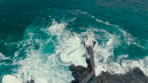 Slowly moving aerial drone video of blue and green ocean sea water hitting the shoreline where steep