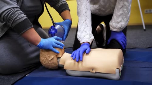 Adults Demonstrating CPR with Bag Valve Mask on Mannequin