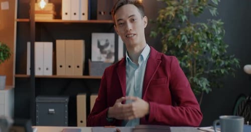 Cheerful Young Businessman Making Online Video Call Looking at Camera and Talking Indoors in Office