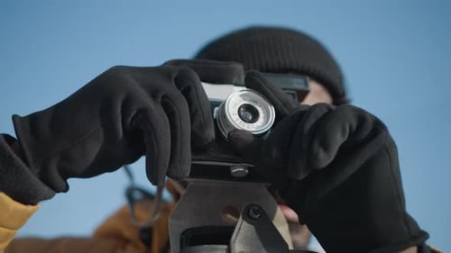 Reporter Adjusting Camera Lens on Snowy Street Under Sunny Sky