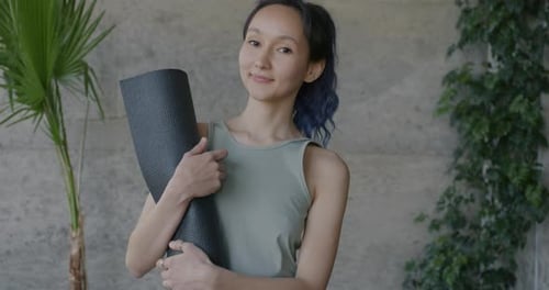 Slow Motion Portrait of Beautiful Asian Woman Standing in Yoga Studio Holding Mat Smiling Looking at