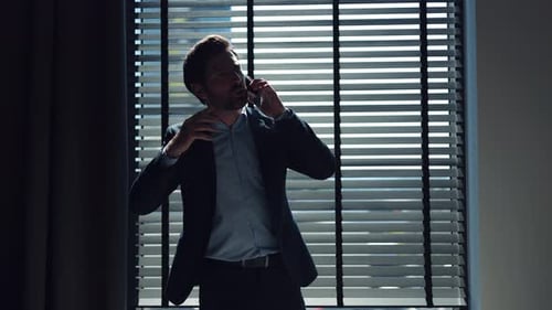 Serious Businessman Talking on Phone Near Window