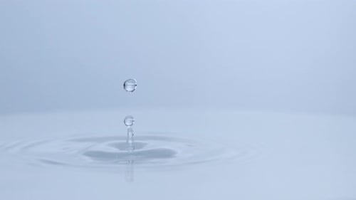 waterdrop falls in clean pool of water creating small circles on the surface. filmed in slow motion