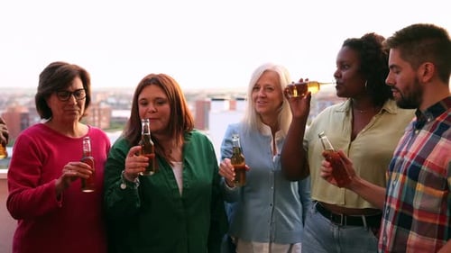 Multiethnic friends having fun cheering with beer at sunset rooftop party. Happy people enjoying hap