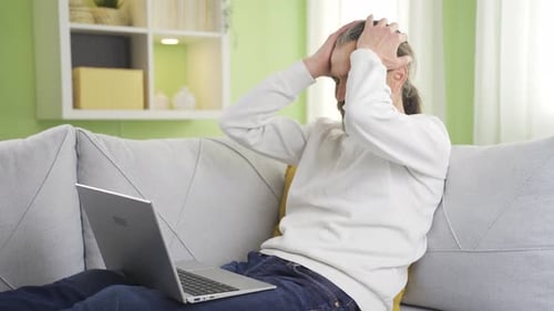 Man On Sofa Using Laptop Appears Frustrated