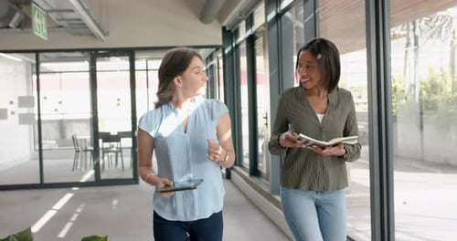 Two diverse businesswomen discussing with each other while walking in office