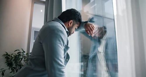 Thoughtful man looks sadly out window in office