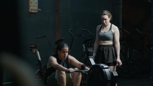 Man Using Rowing Machine with Trainer at Gym