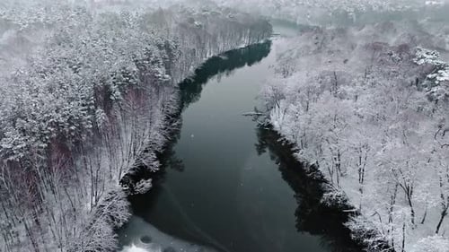 Aerial view of snowy forest and cold river in winter.
