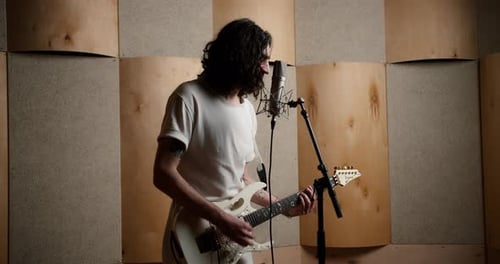 Portrait of a Man Plays Electric Guitar and Sings Into Microphone in Recording Studio