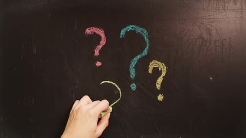 Human Hand Draws Lot of Question Marks with Chalk on Blackboard